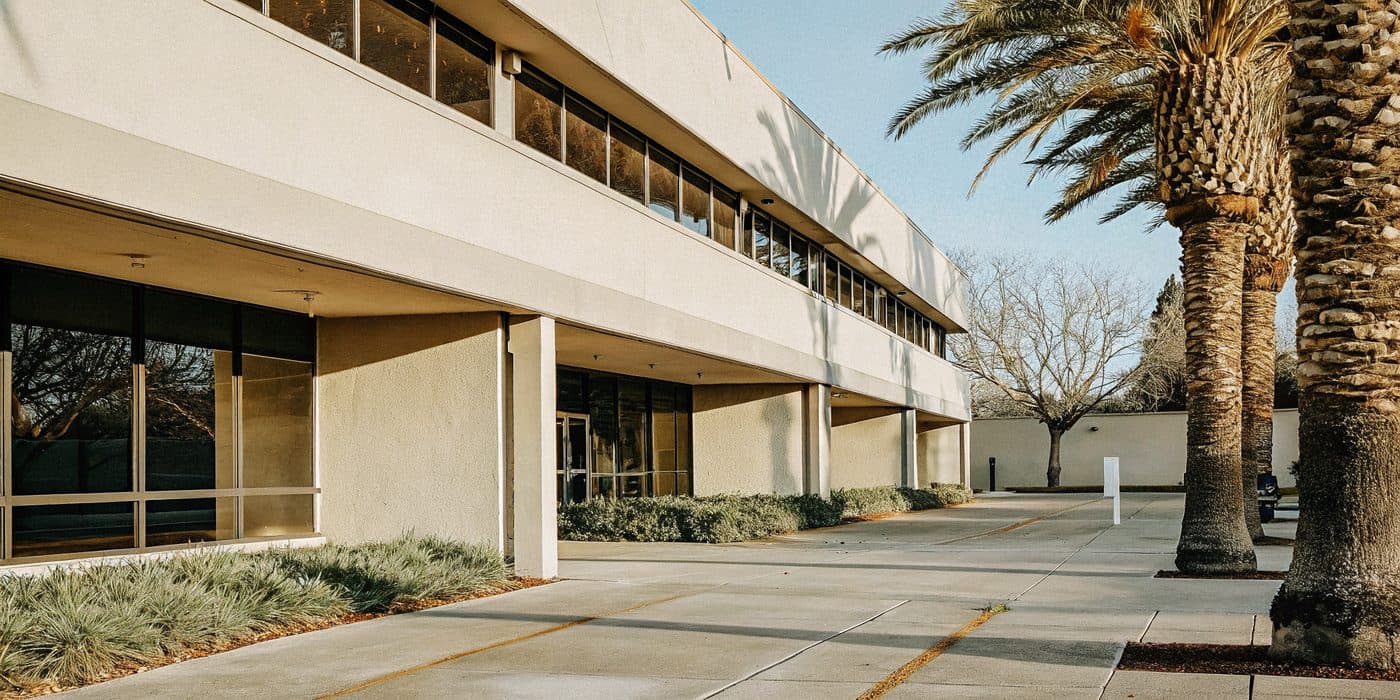 A calm Bay Area office exterior in warm morning light with a palm tree