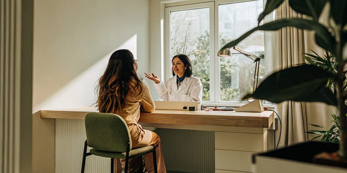 A doctor and patient talking across a desk in a bright, calm consultation room